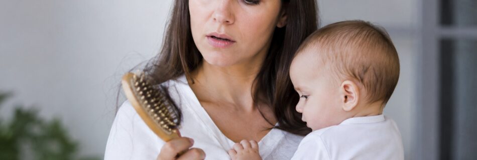 chute de cheveux post partum, jeune maman avec bébé tenant une brosse remplie de cheveux, perte capillaire après grossesse, intérieur lumineux, 2026, format 16/9